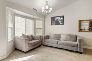 Living area featuring vaulted ceiling, light wood-style flooring, and a chandelier