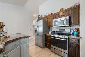 Kitchen featuring stainless steel appliances, light wood-style flooring, and dark stone countertops