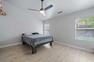 Bedroom featuring vaulted ceiling, multiple windows, light wood-style floors, ceiling fan, and a textured ceiling