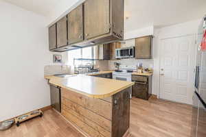 Kitchen with a peninsula, tasteful backsplash, appliances with stainless steel finishes, light wood-style flooring, and light countertops