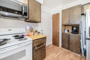 Kitchen featuring white range with electric stovetop, stainless steel microwave, light wood-style flooring, backsplash, and light countertops