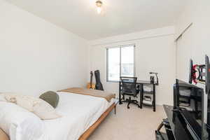 Bedroom featuring light colored carpet, a closet, and a desk