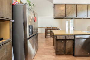 Kitchen with stainless steel appliances, light countertops, light wood finished floors, and dark brown cabinetry