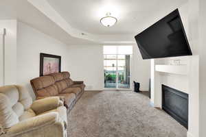 Carpeted living area featuring a fireplace and a raised ceiling