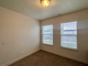 Unfurnished room with a textured ceiling and dark colored carpet