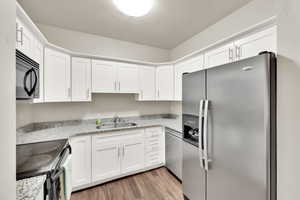 Kitchen featuring black appliances, a textured ceiling, light wood-type flooring, white cabinetry, and light stone countertops