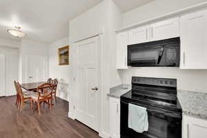 Kitchen with black appliances, white cabinets, light stone countertops, and dark wood-type flooring