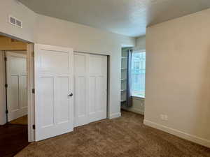 Unfurnished bedroom featuring a textured ceiling, a closet, and dark colored carpet