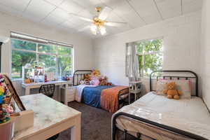 Bedroom with concrete block wall, ceiling fan, and dark colored carpet