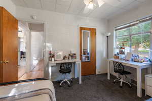 Carpeted bedroom with a desk, a ceiling fan, and concrete block wall