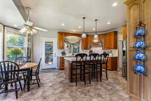 Kitchen featuring a breakfast bar, backsplash, brown cabinets, pendant lighting, and a kitchen island