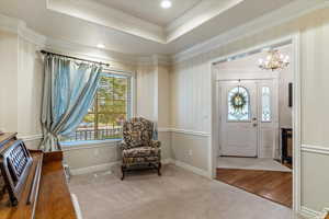 Foyer with a raised ceiling, light colored carpet, a chandelier, ornamental molding, and recessed lighting