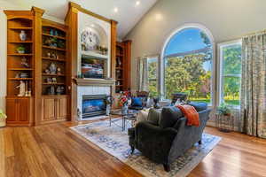 Living area with a fireplace, light wood-type flooring, recessed lighting, high vaulted ceiling, and built in shelves
