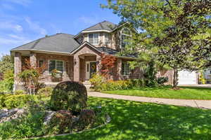 Traditional-style home featuring a porch, brick siding, a front lawn, and a shingled roof