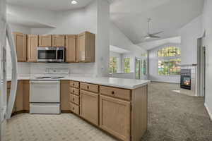 Kitchen featuring white range with electric stovetop, a peninsula, light brown cabinetry, open floor plan, and stainless steel microwave