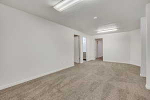 Carpeted empty room featuring a textured ceiling and baseboards