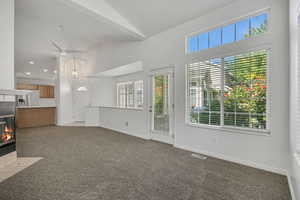 Unfurnished living room with a tile fireplace, light colored carpet, healthy amount of natural light, and high vaulted ceiling