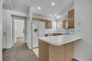 Kitchen with light countertops, white appliances, a peninsula, lofted ceiling, and recessed lighting