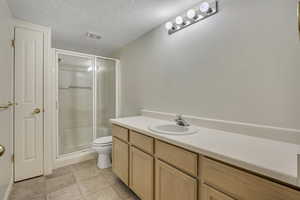 Full bathroom featuring a textured ceiling, vanity, a stall shower, and light tile patterned floors
