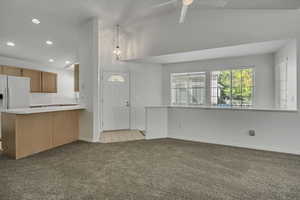 Kitchen with a peninsula, light carpet, light countertops, recessed lighting, and white refrigerator with ice dispenser