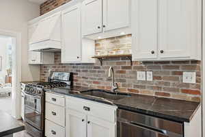 Kitchen with appliances with stainless steel finishes, white cabinetry, custom range hood, and open shelves