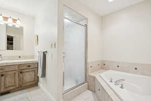 Bathroom featuring light tile patterned flooring, a shower stall, a garden tub, and vanity