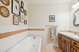 Full bath with a freestanding tub, light tile patterned floors, vanity, tile walls, and a wainscoted wall