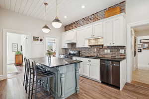 Kitchen featuring pendant lighting, stainless steel appliances, a kitchen bar, white cabinetry, and light wood-type flooring