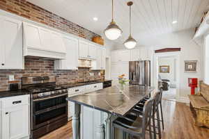 Kitchen featuring a breakfast bar, appliances with stainless steel finishes, decorative light fixtures, a kitchen island, and white cabinetry