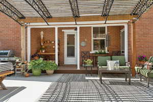 View of exterior entry featuring brick siding, a pergola, and a patio area