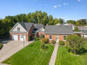 View of front facade with a front yard, driveway, roof with shingles, a garage, and brick siding