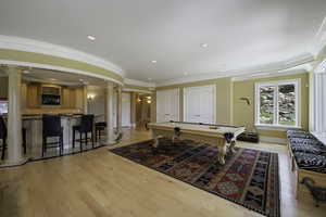 Rec room featuring ornate columns, healthy amount of natural light, ornamental molding, light wood-style floors, and billiards