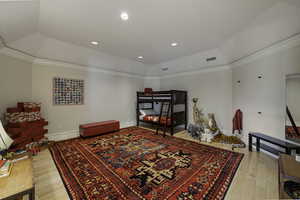 Bedroom featuring light wood-style floors, lofted ceiling, crown molding, recessed lighting, and a raised ceiling