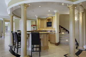 Kitchen with decorative columns, dark stone countertops, light brown cabinetry, a kitchen bar, and recessed lighting