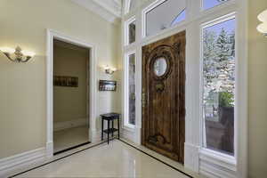 Foyer entrance featuring inlaid floor details, healthy amount of natural light, ornamental molding, and light tile patterned floors