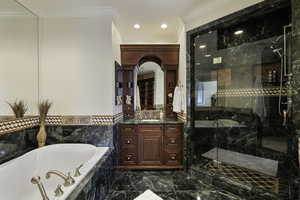 Full bath with a garden tub, dark marble finish floors, crown molding, vanity, and a marble finish shower