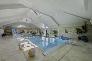 Indoor pool with a water slide, a skylight, and a diving board