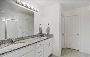 Full bathroom with double vanity, light tile patterned floors, and a shower stall