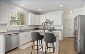 Kitchen featuring stainless steel appliances, white cabinets, light stone countertops, a kitchen breakfast bar, and light wood-style flooring