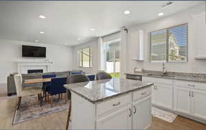 Kitchen featuring a kitchen breakfast bar, white cabinetry, light stone counters, light wood-type flooring, and recessed lighting