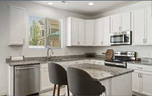 Kitchen featuring appliances with stainless steel finishes, light stone countertops, white cabinets, a center island, and a kitchen breakfast bar