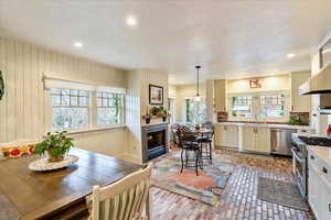 Kitchen with brick flooring, appliances with stainless steel finishes, a textured ceiling, a warm lit fireplace, and light countertops