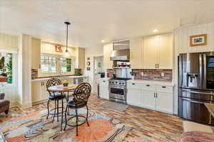 Kitchen with appliances with stainless steel finishes, brick flooring, wood walls, pendant lighting, and cream cabinetry
