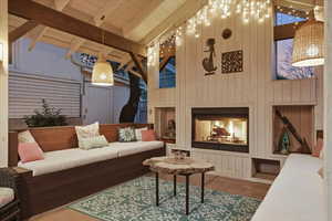Living room with a fireplace, high vaulted ceiling, wood walls, and a wood ceiling with exposed beams