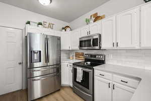 Kitchen featuring appliances with stainless steel finishes, white cabinets, light wood-type flooring, and a textured ceiling