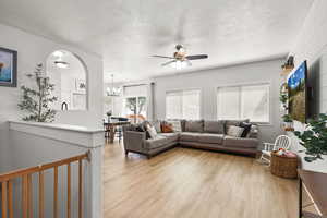 Living area with light wood finished floors, a textured ceiling, ceiling fan, plenty of natural light, and a chandelier