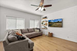 Living area featuring a textured ceiling, light wood-type flooring, a ceiling fan, and wooden walls