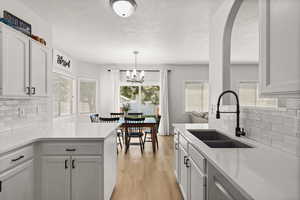 Kitchen featuring backsplash, a peninsula, a textured ceiling, white cabinets, and light stone counters