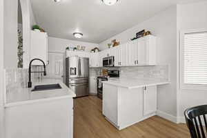Kitchen with stainless steel appliances, white cabinets, backsplash, light wood-type flooring, and light stone countertops