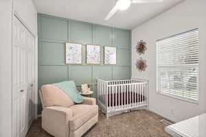 Carpeted bedroom featuring a decorative wall, a ceiling fan, a closet, and a nursery area